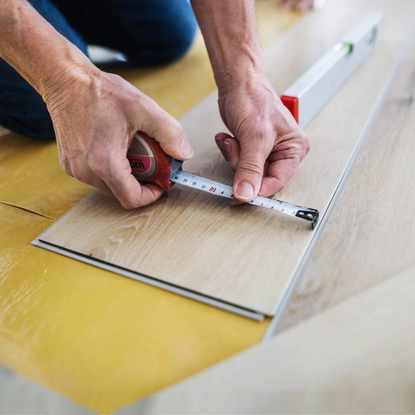 Person measuring a light wood plank with a tape measure.